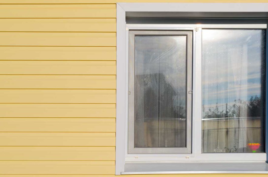 A close shot of sound blocking windows on a yellow house from outside under the sun